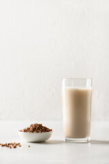 Buckwheat milk served in drinking glass with grain ingredient on a white background. Concept healthy lactose free and plant based vegan milk replacer. Vertical format.