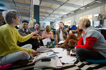 Team sitting on office floor, discussing paperwork