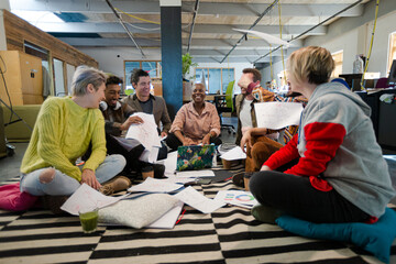 Team sitting on office floor, discussing paperwork