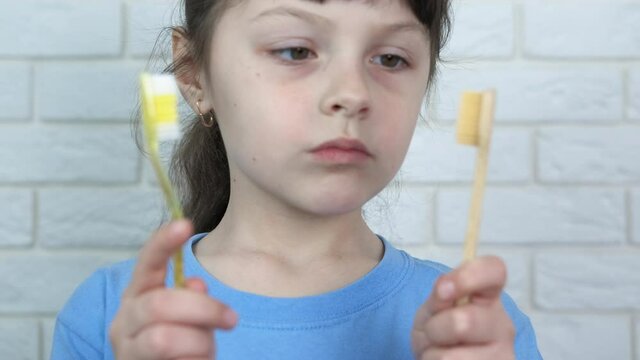 Choosing a toothbrush. A little girl chooses between a plastic and a bamboo toothbrush. Choosing a dental eco-brush.
