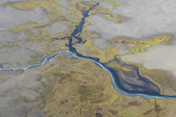 Aerial photograph of braided river in Iceland, with two colors of water meeting. Background of brown and green.