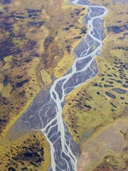 Aerial photo of a braided river on a barren green and brown landscape. 