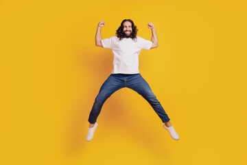 Fototapeta na wymiar Portrait of astonished excited active guy jump hold fists on yellow background