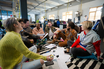 Team sitting on office floor, discussing paperwork