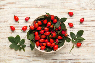 Ripe rose hip berries with green leaves on white wooden table, flat lay