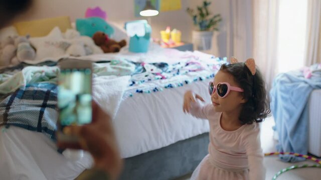 happy little girl playing dress up dancing in bedroom with mother taking photo using smartphone sharing on social media