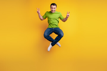 Fototapeta na wymiar Portrait of funky cheerful friendly guy jump sport raise hand show v-sign on yellow wall