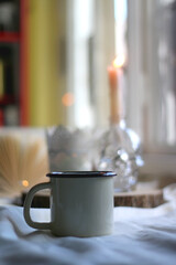 Cup of hot drink, open book and lit candles on a table. Hygge at home. Selective focus.