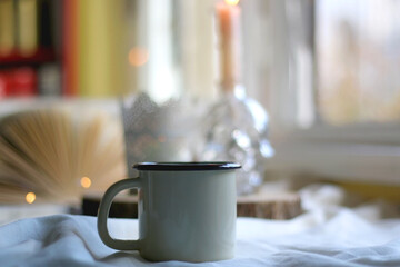 Cup of hot drink, open book and lit candles on a table. Hygge at home. Selective focus.