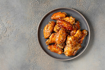 Homemade baked or fried chicken wings in barbecue sauce in a plate on the cooking table top view	