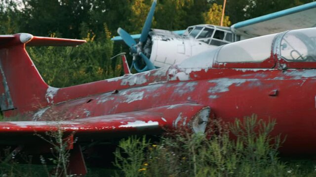 Old Delfin L-29 training aircraft with chipped red paint on fuselage near Antonov-2 plane on field of abandoned aerodrome on summer day