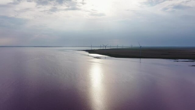 A wind farm on the shores of a pink lake at sunset. Lake Lemuria or Pink Lake is a lake in the Kherson region of Ukraine. Aerial view
