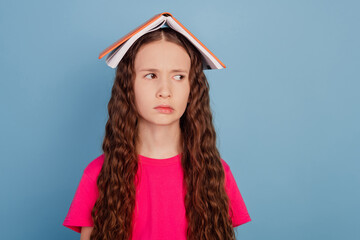 Portrait of unhappy tired little lady look empty space book on head on blue background
