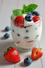 Yogurt with strawberries and blueberries in a glass, on a rustic wooden table.