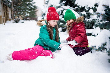 Wintertime. Cute girls playing with snow, building an igloo. Siblings having fun outside on snow day. Awesome winter outdoor activities for kids concept