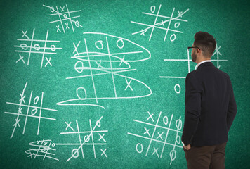 Young businessman near green chalkboard with drawn tic tac toe game
