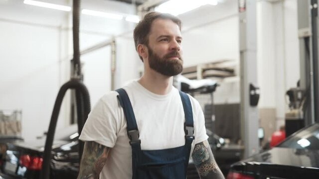 Bearded tattooed auto mechanic man walking in the garage indoors