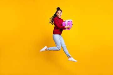Fototapeta na wymiar Full length photo of charming cute dark skin lady wear red pullover smiling jumping giving present isolated yellow color background