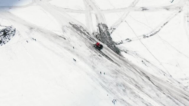 Aerial view red modern snowcat ratrack descends from the slopes of the mountain along a rolled road on a glacier to the base camp bypassing climbers