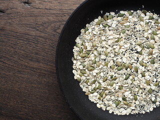 Mixed seed in black pan: oats, pumpkin seed, sunflower seed and black and white sesame seed