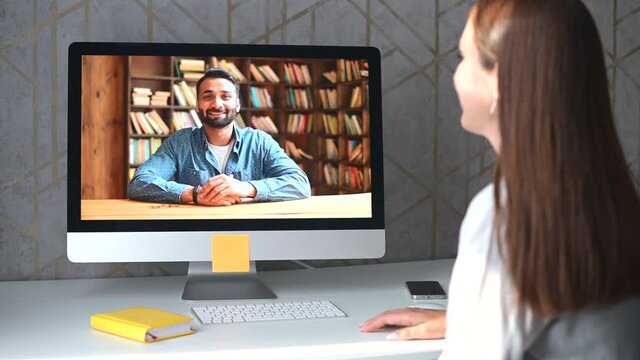 Young woman talking online with an Indian man, support service representative or colleague via video connection on the laptop, female using computer app for virtual communication, rear view, 4k