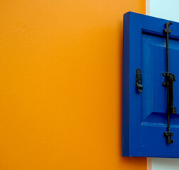 Deeep blue wooden window shutter on bright orange and white wall, color compbination in outdoor architecture design
