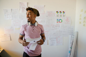 Young man holding paperwork in office, smiling