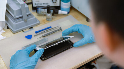 Phone repair concept a broken screen being removed from the body of the smartphone carefully with the tools on the wooden desk