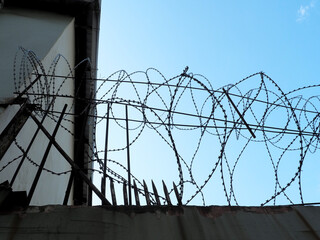 Fragment of an old concrete fence with barbed wire at the top against the blue sky
