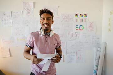 Young man holding paperwork in office, smiling