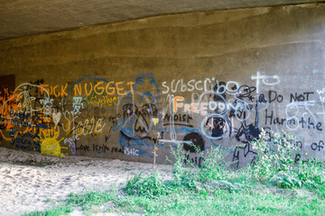 Vandals spray-paint graffiti on concrete bridge footing.
