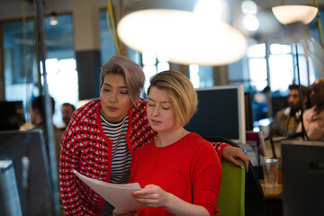 Young women discussing paperwork at computer