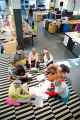 Team sitting on office floor, discussing paperwork