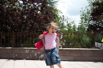 The little girl is in the garden of her house, trying to catch the bubbles. selective focus girl.