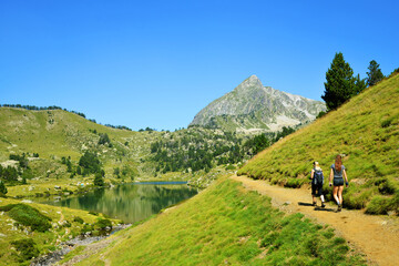 Fototapeta na wymiar Hikers on a trip in Neouvielle national nature reserve, Lac du Milieu, French Pyrenees. Beautiful summer mountain landscape in the sunny day.