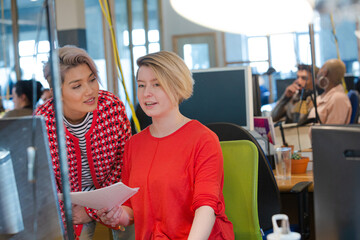 Young women discussing paperwork at computer