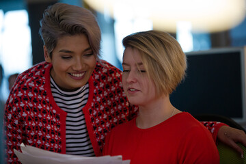 Young women discussing paperwork at computer