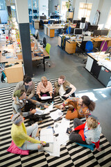 Team sitting on office floor, discussing paperwork