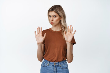 Fototapeta na wymiar Young woman rejecting something, raising hands in stop gesture, say no, refusing or declining, standing over white background