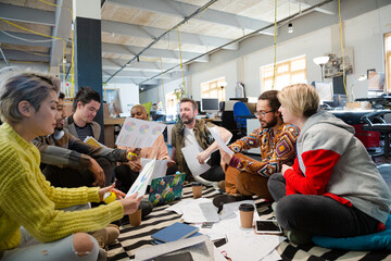 Team sitting on office floor, discussing paperwork