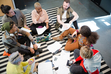 Team sitting on office floor, discussing paperwork