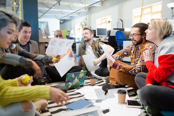 Team sitting on office floor, discussing paperwork