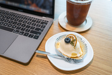 Close-up of ice coffee in cup mug and Homemade white orange cake ​with keyboard  laptop computer on wood desk office desk in coffee shop at the cafe,during business work concep