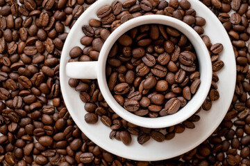 white coffee cup with roasted beans lies among coffee beans background. Top view with copy space for your text