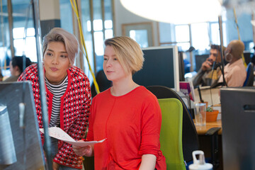 Fototapeta premium Young women discussing paperwork at computer