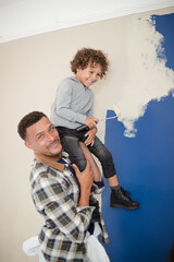 Portrait happy father and son with paint rollers painting room