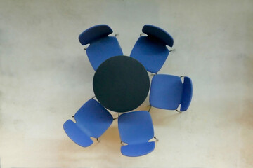 Empty round black table with blue seats on the concrete floor. Top view.