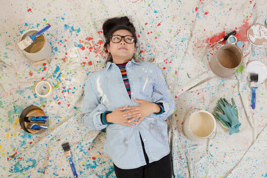 Woman Taking A Break From Painting, Laying On Dropcloth Among Paint Cans