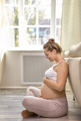 Pregnant woman caressing her belly at home.