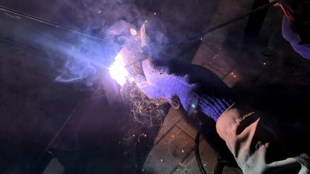 Process of electric welding of metal structures. Bright flames, smoke and sparks. Master in work gloves.